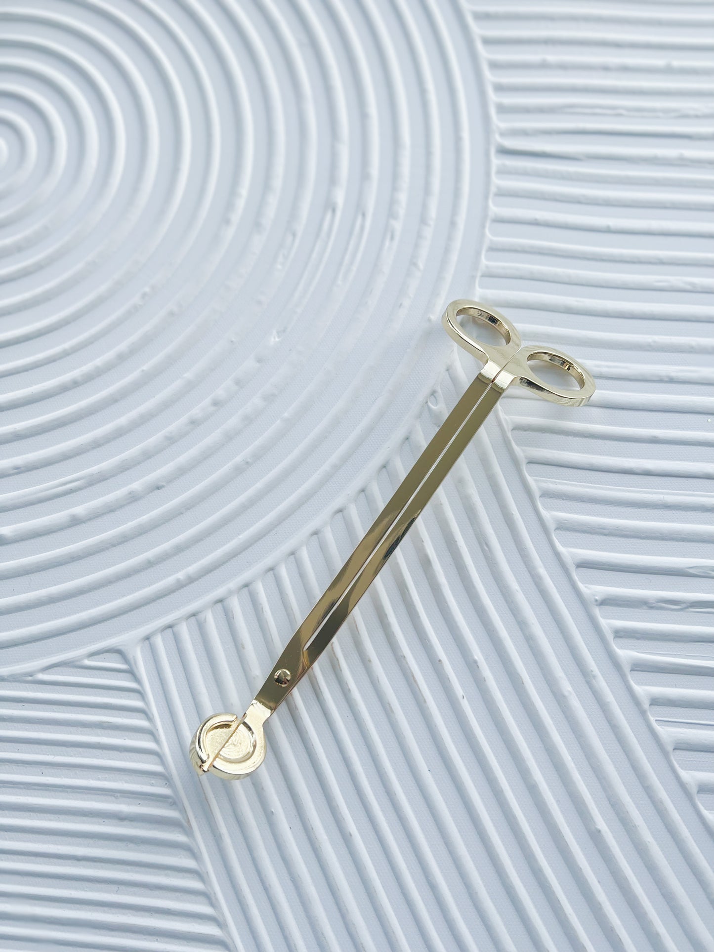 a gold wick trimmer on a textured, white surface